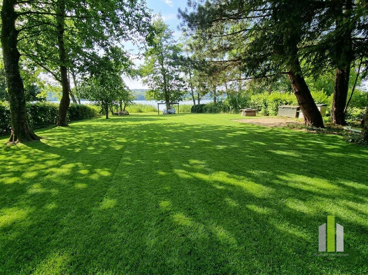 Weitläufiger, gepflegter Garten mit altem Baumbestand, der Schatten spendet, und direktem Blick auf den See.