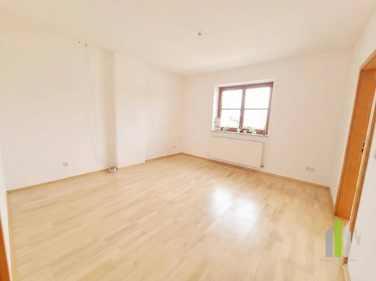 Leeres Zimmer mit hellem Holzboden, weißen Wänden und einem Fenster mit Holzrahmen.