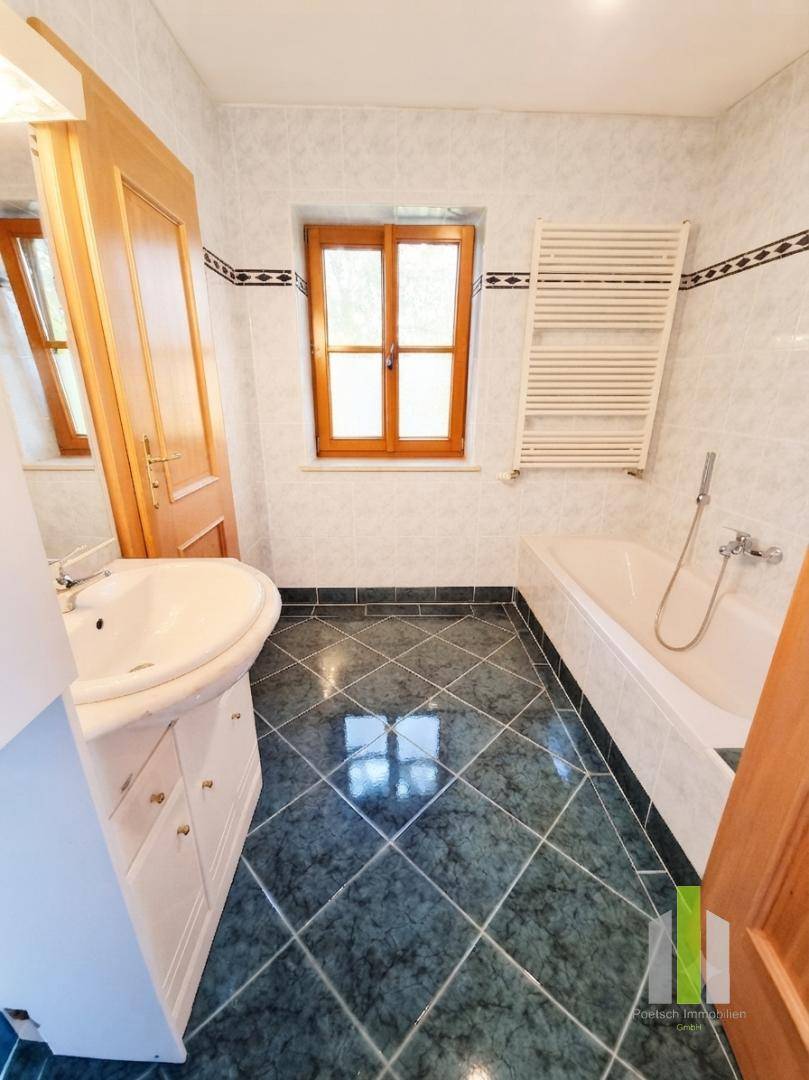 Badezimmer mit grünen Bodenfliesen, Badewanne, Waschbecken, Fenster und Handtuchheizkörper.