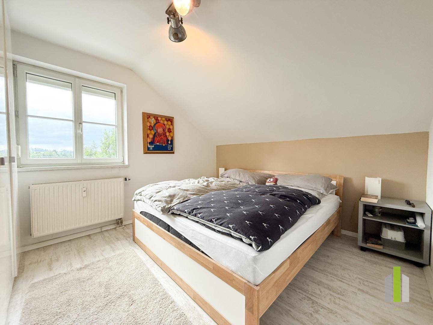 Helles Schlafzimmer mit Dachschräge, großem Fenster und hellem Laminatboden.