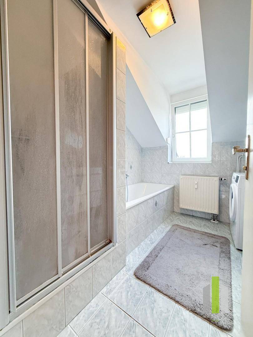 Badezimmer mit Dusche, Badewanne unter der Dachschräge und Fenster für Tageslicht.