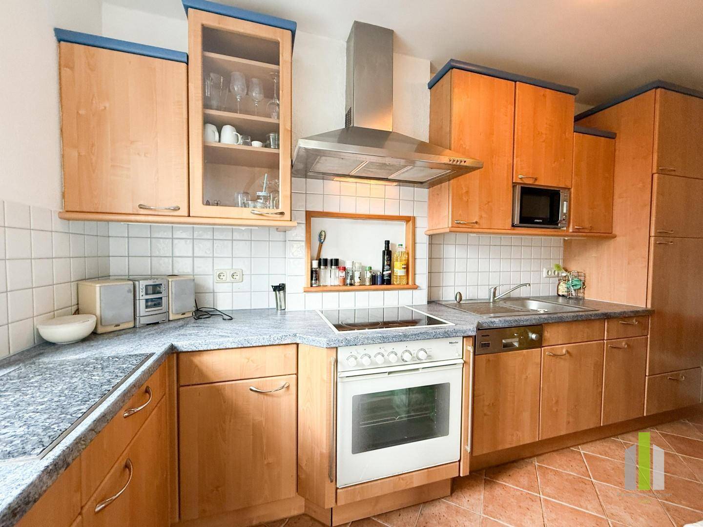 Funktionale Küche mit Holzschränken, Granit-Arbeitsplatten und integrierten Geräten.