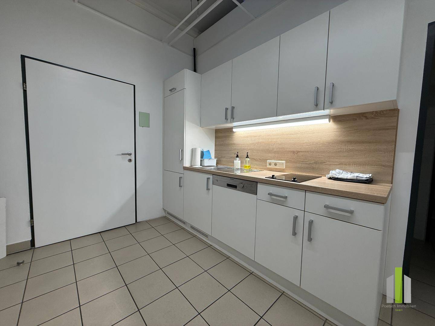 Funktionale Küchenzeile mit weißen Schränken, Holzoptik-Arbeitsplatte und Fliesenboden.