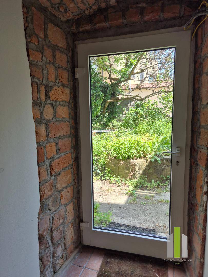 Ausgang zu einem grünen Gartenbereich mit einer Glastür, umgeben von rustikalen Ziegelwänden.