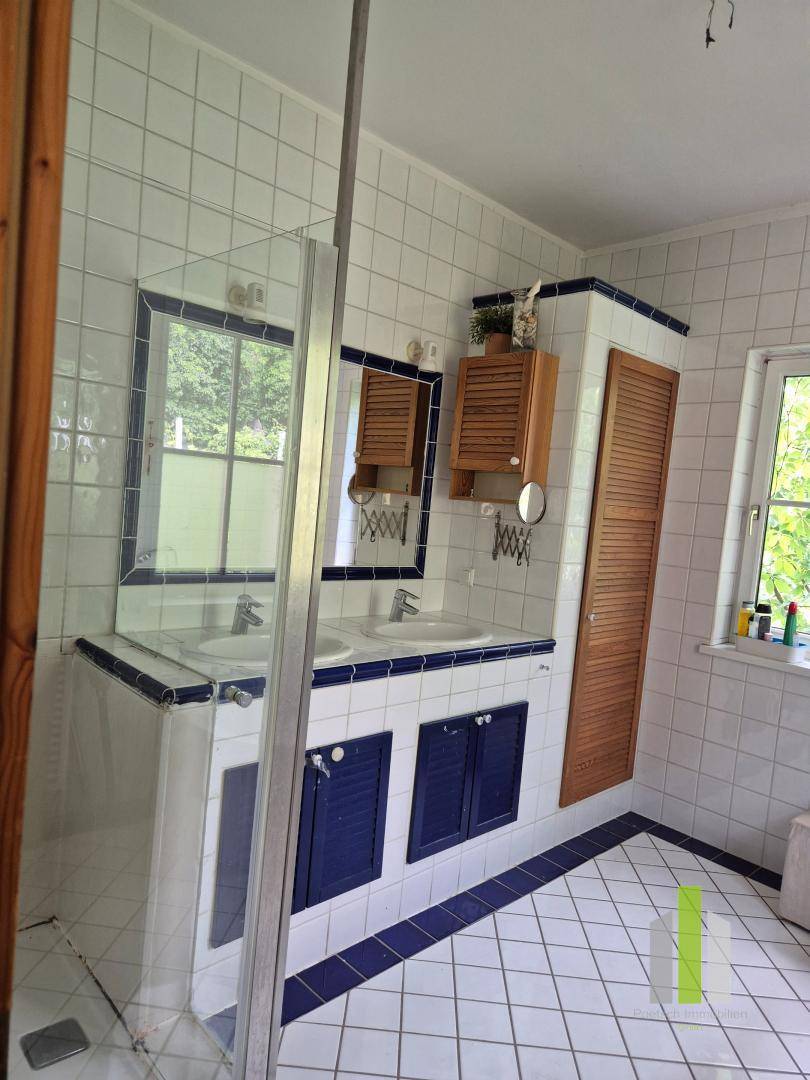 Badezimmer mit weißen Fliesen, blauen Akzenten, Doppelwaschbecken und Duschkabine.