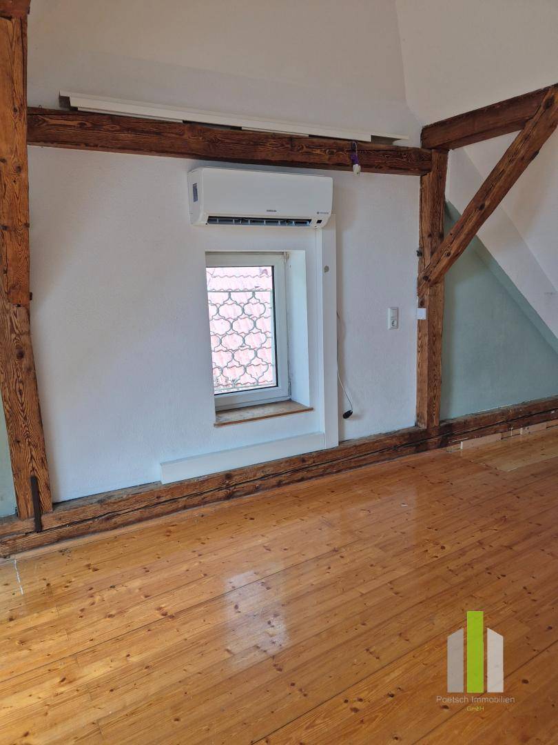 Dachzimmer mit Holzbalken, Holzboden und Klimaanlage, ideal als Schlaf- oder Arbeitszimmer.