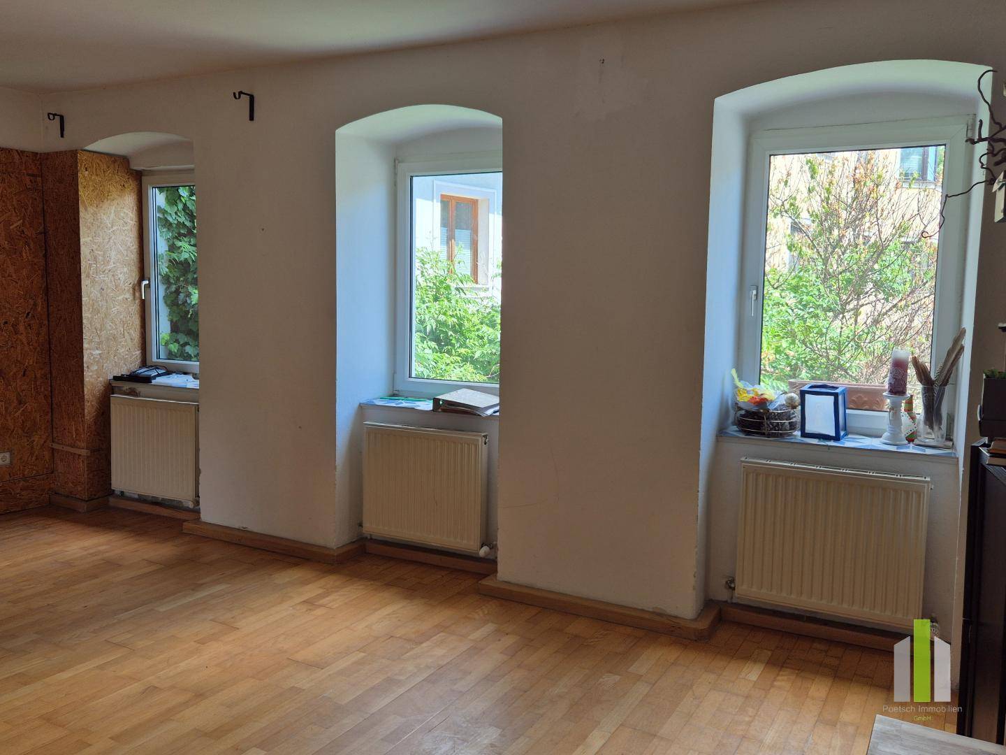 Geräumiges Wohnzimmer mit Holzboden und drei Fenstern, die viel Tageslicht hereinlassen.