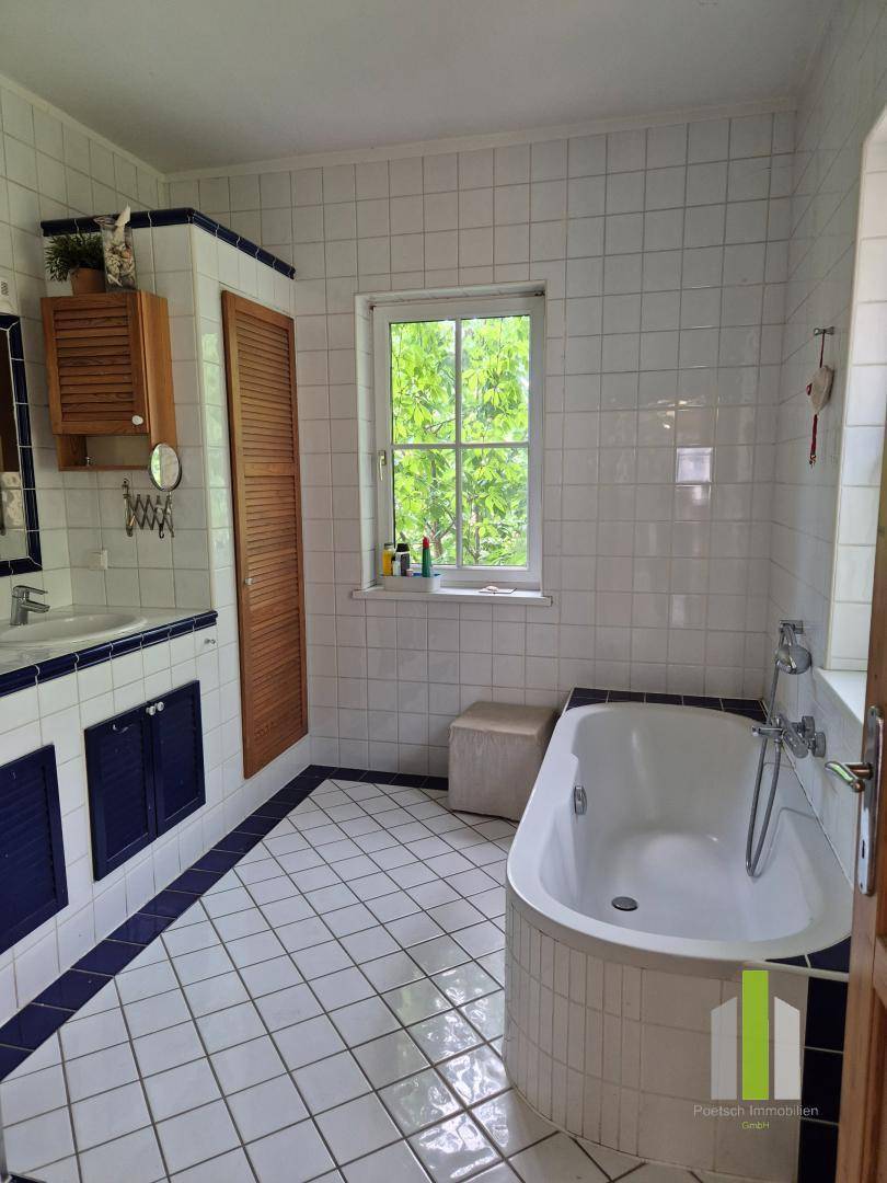 Badezimmer mit weißen Fliesen, blauen Akzenten, Badewanne und Fenster mit Blick ins Grüne.
