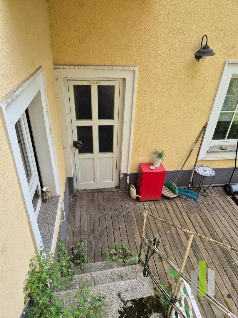Holzterrasse mit Zugang zum Haus und Stufen, umgeben von einer gelben Fassade.