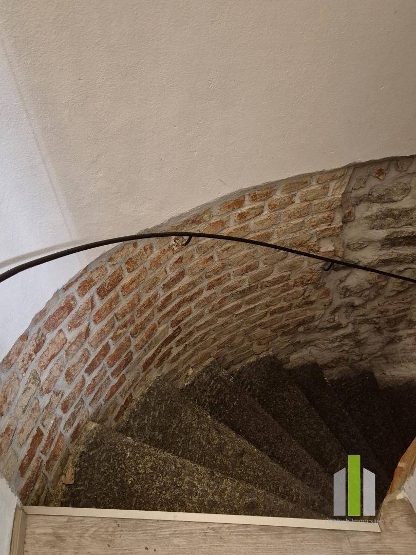 Historische Wendeltreppe mit Steinstufen, schmiedeeisernem Geländer und freigelegter Ziegelwand.