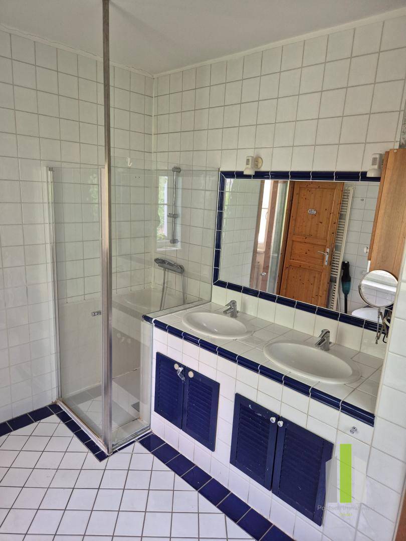 Badezimmer mit Doppelwaschbecken, Duschkabine und weißen Fliesen mit blauen Bordüren.