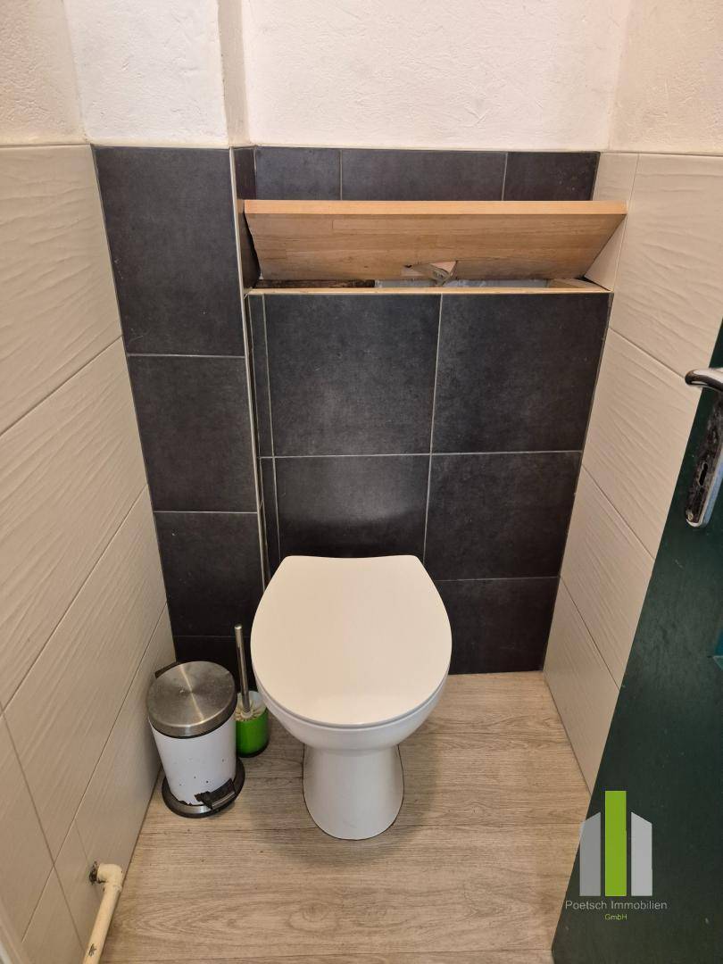 Kleine Toilette mit dunklen und hellen Fliesen sowie einem wandhängenden WC.