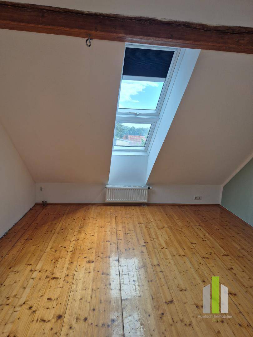 Geräumiges Dachzimmer mit Holzboden, Dachschrägen und zwei großen Dachfenstern für helle Atmosphäre.
