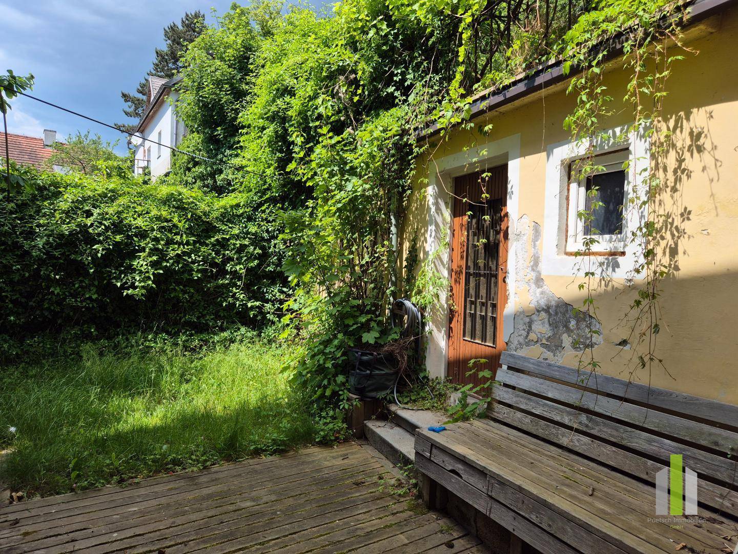 Gemütlicher Gartenbereich mit Holzterrasse, integrierter Sitzbank und üppiger grüner Hecke.