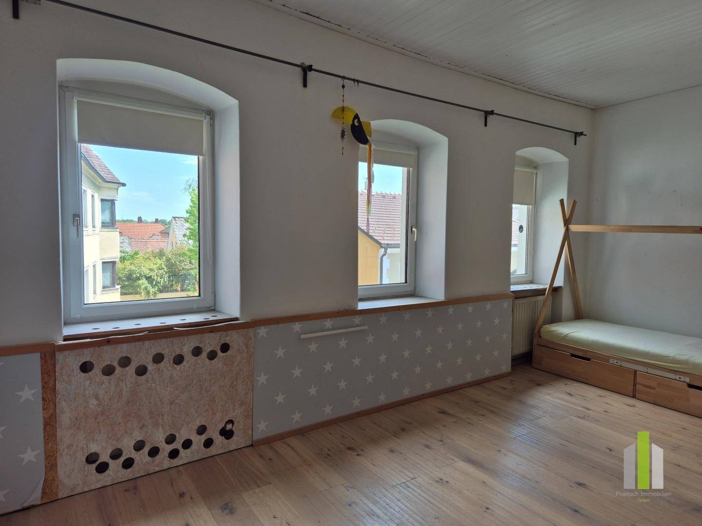 Helles Kinderzimmer mit Holzboden, mehreren Fenstern und einer Holzkonstruktion.