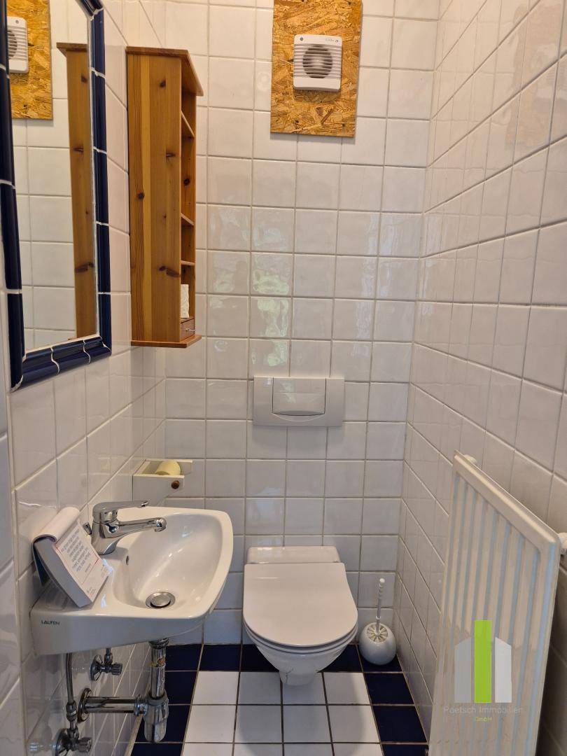 Kleines Badezimmer mit WC, Waschbecken und weißen Fliesen mit blauen Akzenten.