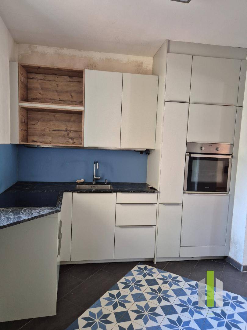 Moderne Küche mit weißen Schränken, dunkler Arbeitsplatte und blauer Rückwand.