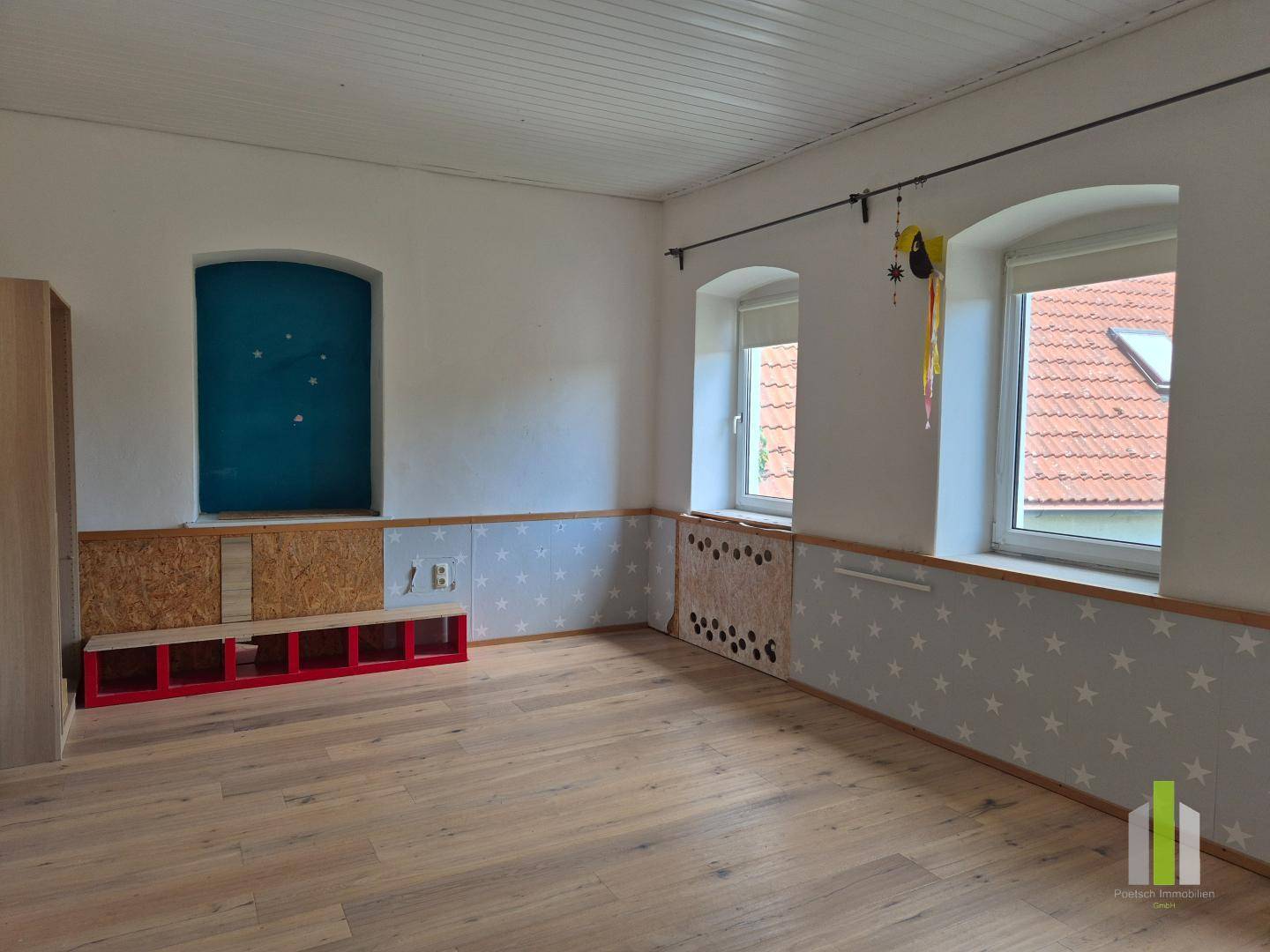 Geräumiges Kinderzimmer mit Holzboden, Sternenmuster-Tapete und einem blauen Nischenfenster.