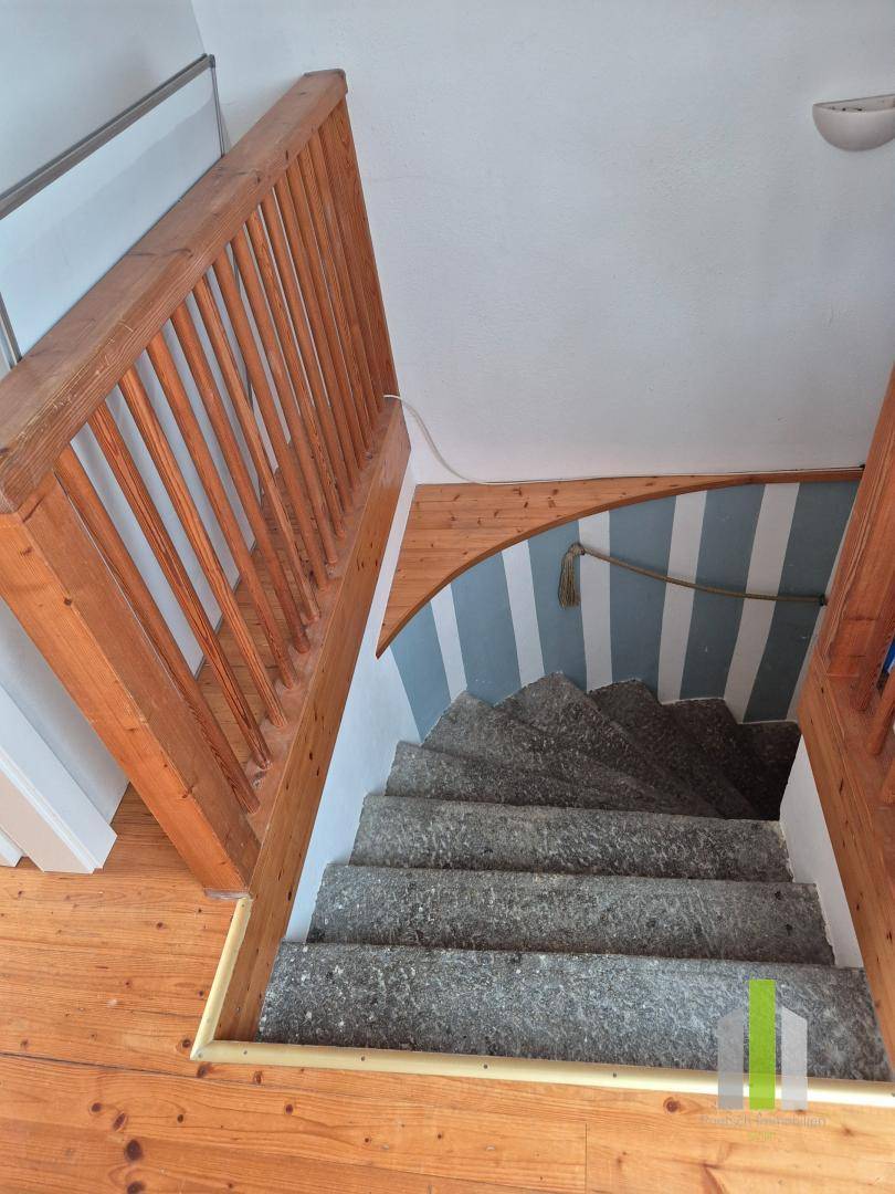 Steintreppe mit Holzgeländer und gestreifter Wandgestaltung, die zu den oberen Etagen führt.