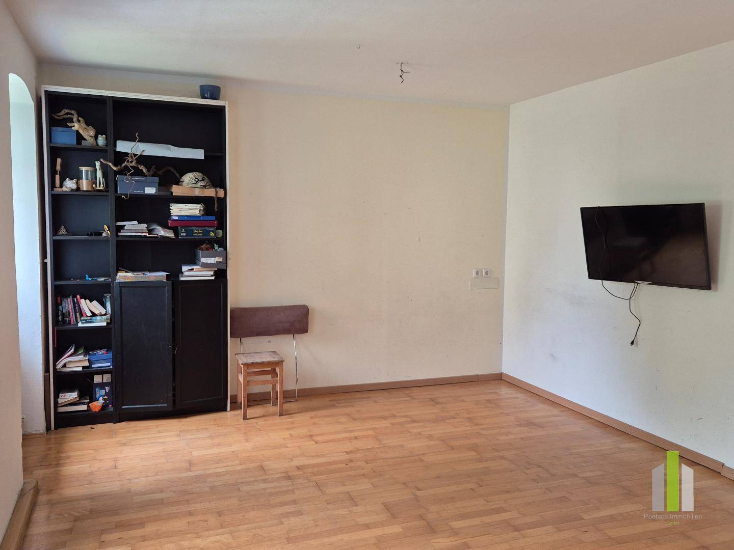 Wohnzimmer mit Holzboden, Bücherregal und einem an der Wand montierten Fernseher.