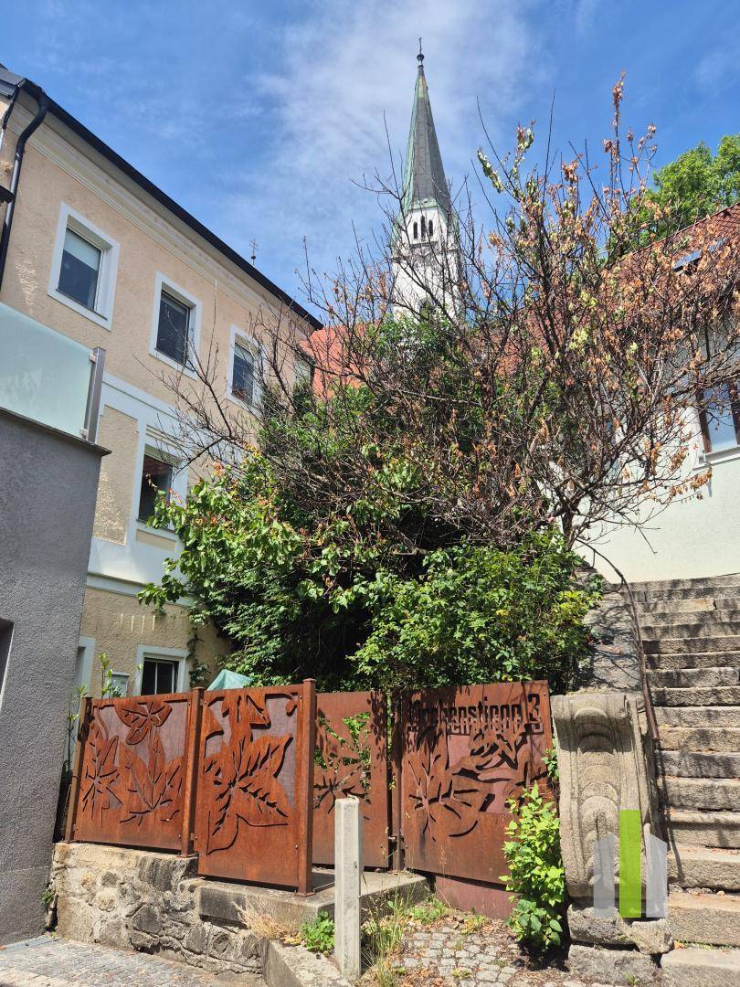 Historische Gasse mit einem Gebäude, dekorativem Metallzaun und Blick auf einen Kirchturm.