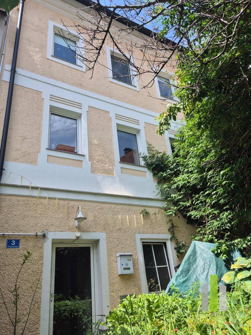 Charmante gelbe Hausfassade mit mehreren Fenstern, umgeben von üppiger Vegetation.