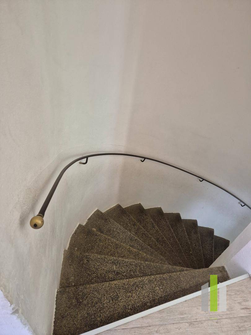 Wendeltreppe mit Steinstufen und schlichtem Metallgeländer in einem historischen Gebäude.