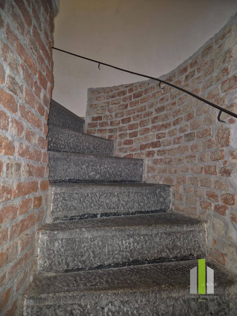 Rustikale Steintreppe mit freigelegten Ziegelwänden und einem schlichten Metallgeländer.