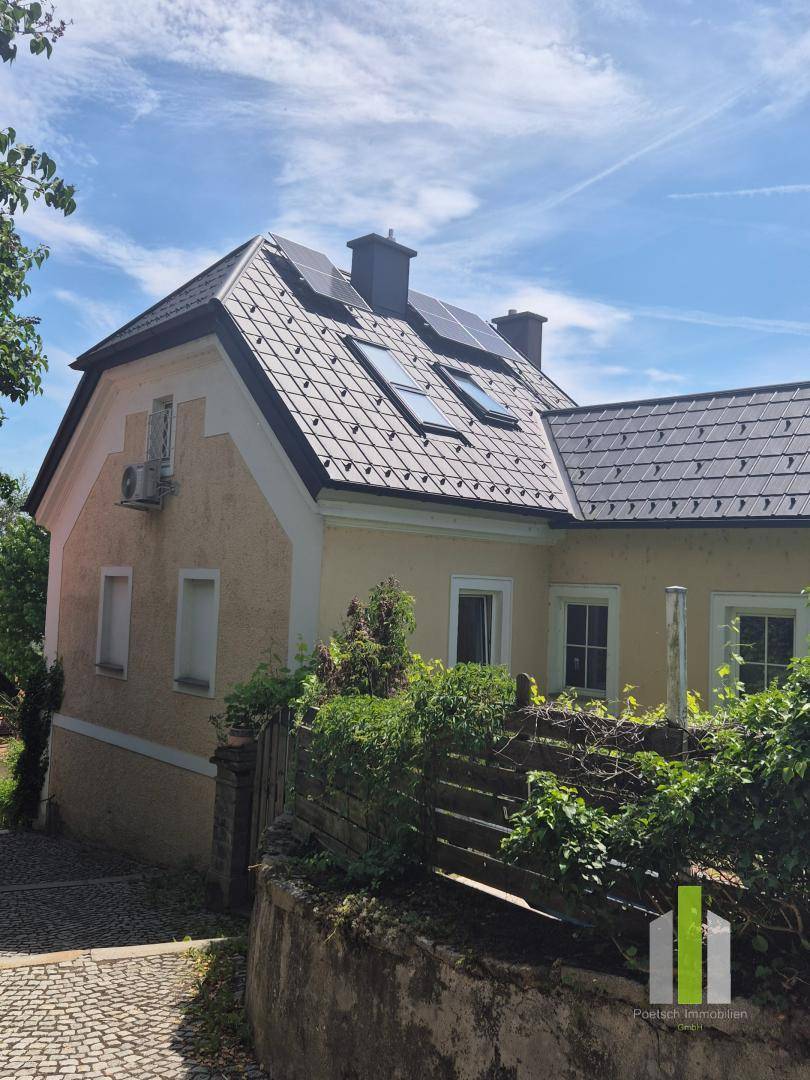 Haus mit gelber Fassade, dunklem Ziegeldach, Dachfenstern und Photovoltaikanlage.