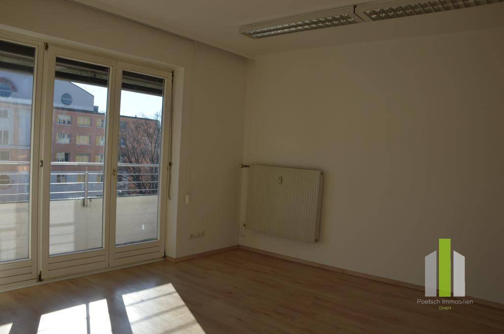 Heller Wohnbereich mit großem Fenster zum Balkon und einem Heizkörper an der Wand.