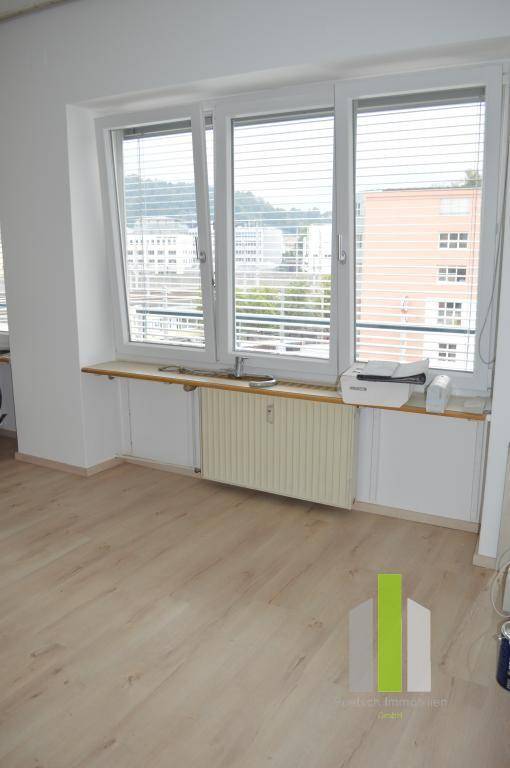Heller Raum mit großen Fenstern und Jalousien, bietet einen weiten Blick über die Stadt.