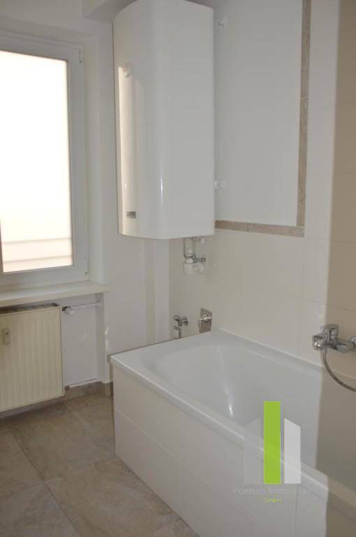 Helles Badezimmer mit Badewanne, Fenster und Wandfliesen, ausgestattet mit Warmwasserboiler.