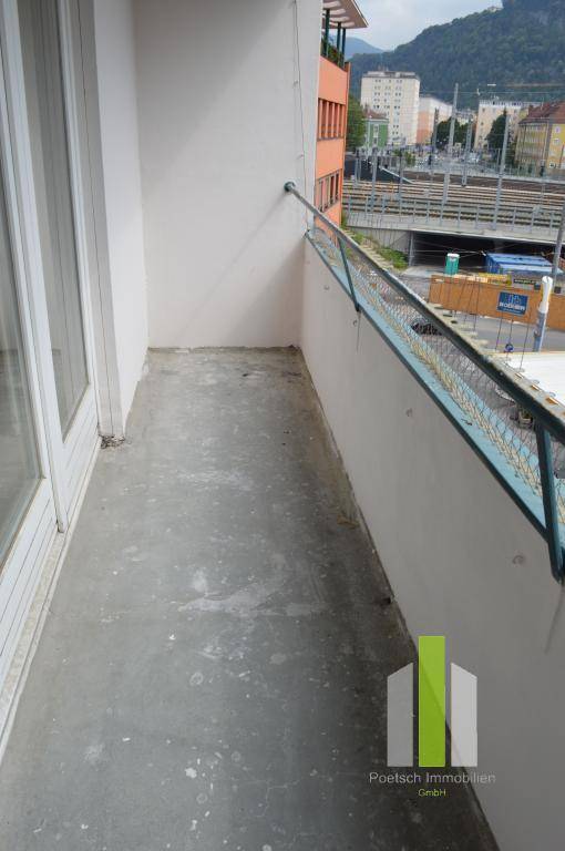 Schmaler Balkon mit Betonboden und Metallgeländer, bietet einen Blick auf die städtische Umgebung.