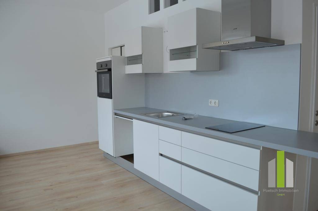Moderne Einbauküche mit weißen Fronten, grauer Arbeitsplatte und integrierten Geräten, sehr hell.