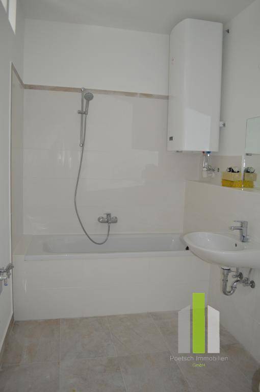 Gefliestes Badezimmer mit Badewanne, Duschfunktion und Waschbecken, inklusive Warmwasserboiler.