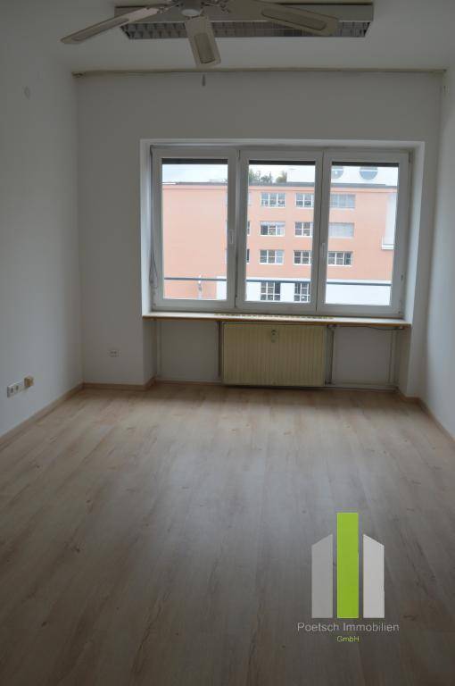 Geräumiger Raum mit Laminatboden, großem Fenster und Deckenventilator, bietet viel Licht.