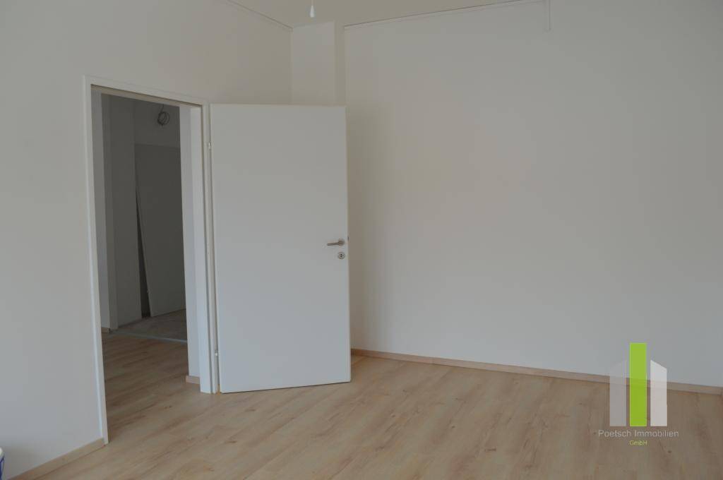 Heller Raum mit Laminatboden und weiß gestrichenen Wänden, bietet Zugang zu weiteren Zimmern.