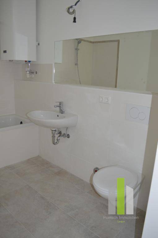 Modernes WC mit Wand-WC, Waschbecken und großem Spiegel, in hellen Fliesen gehalten.