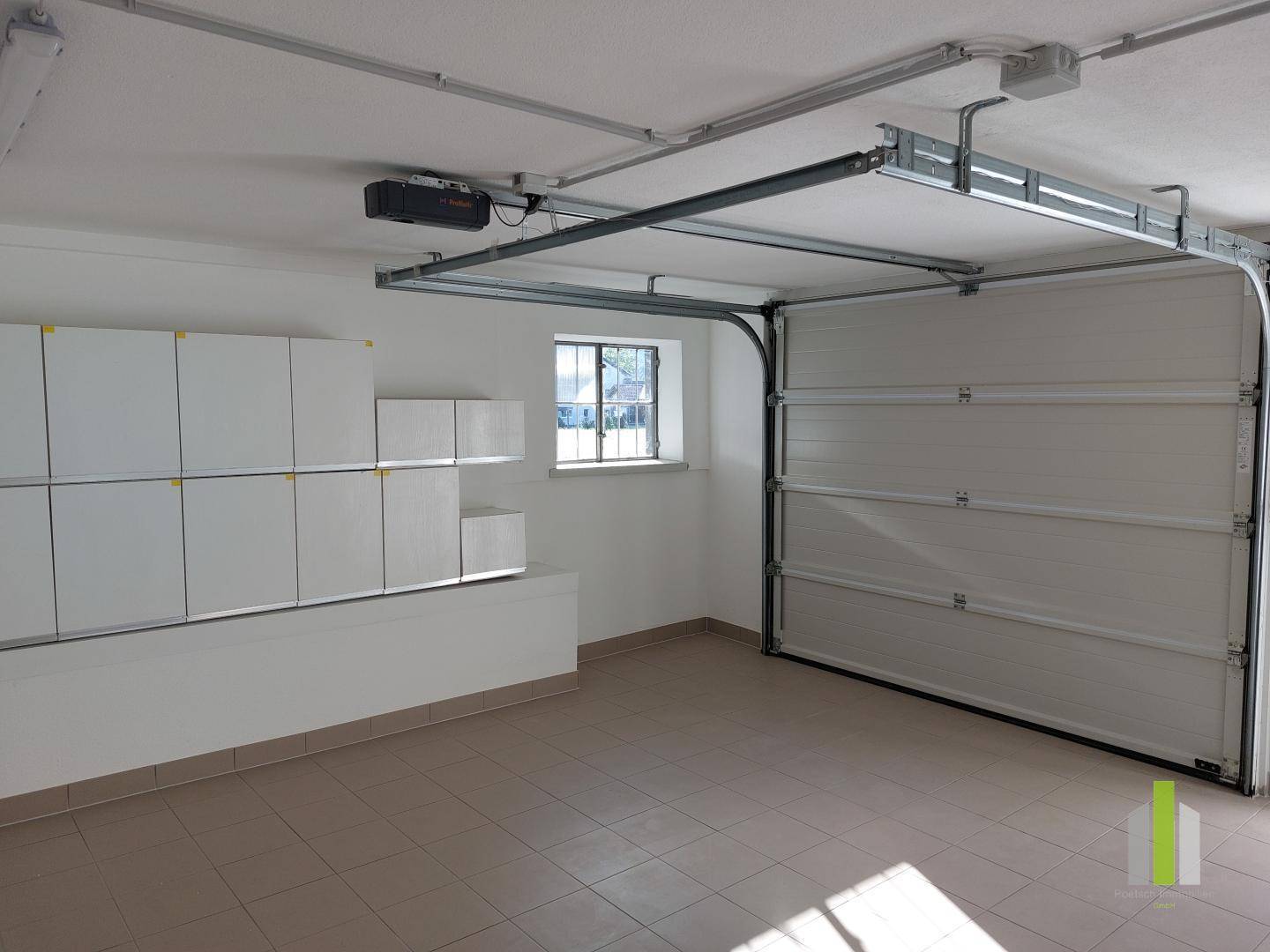 Saubere und helle Garage mit Fliesenboden, Fenster und praktischen Wandregalen.