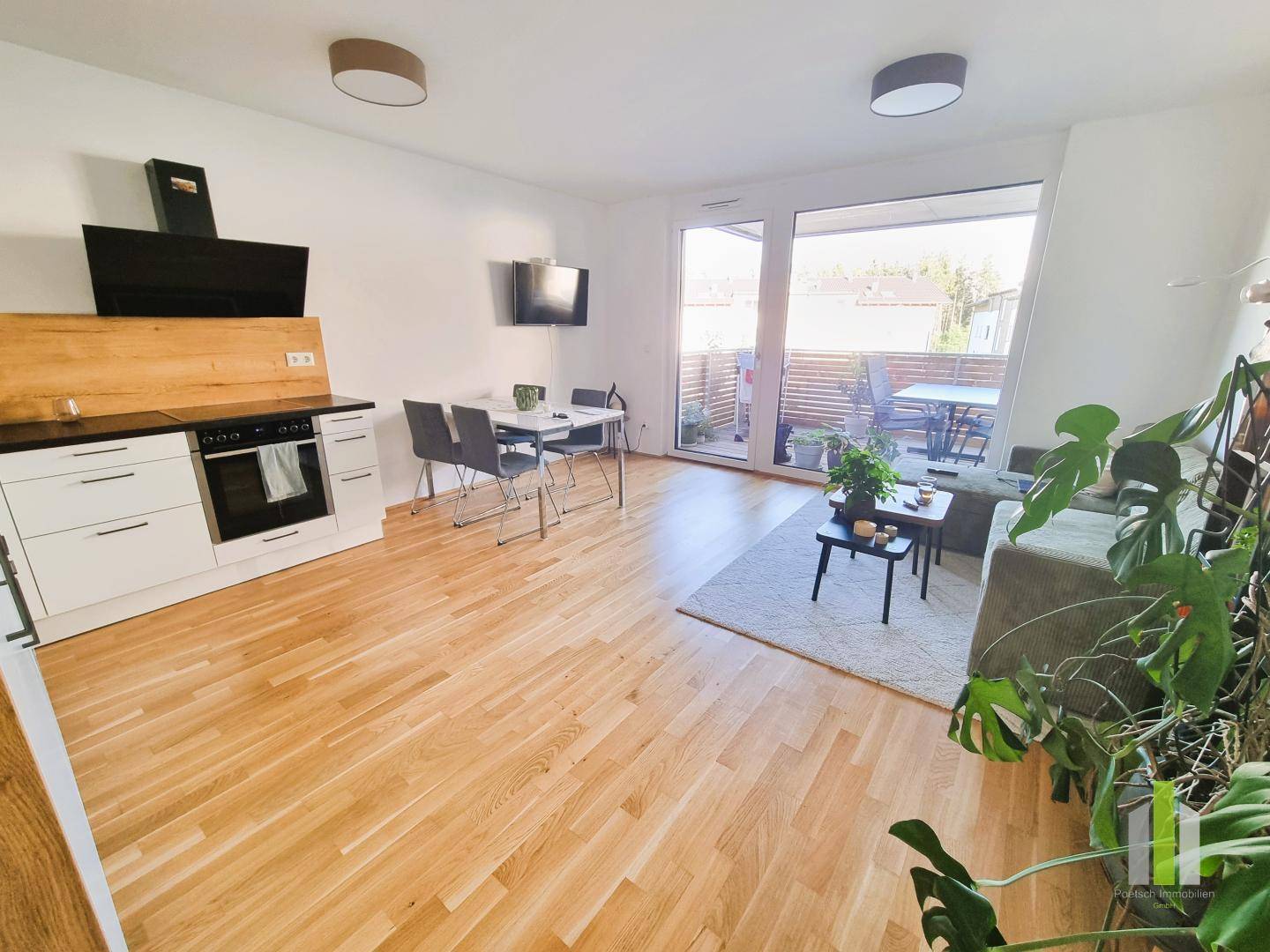 Heller offener Wohn-Essbereich mit moderner Einbauküche, Holzboden und direktem Zugang zur Terrasse.
