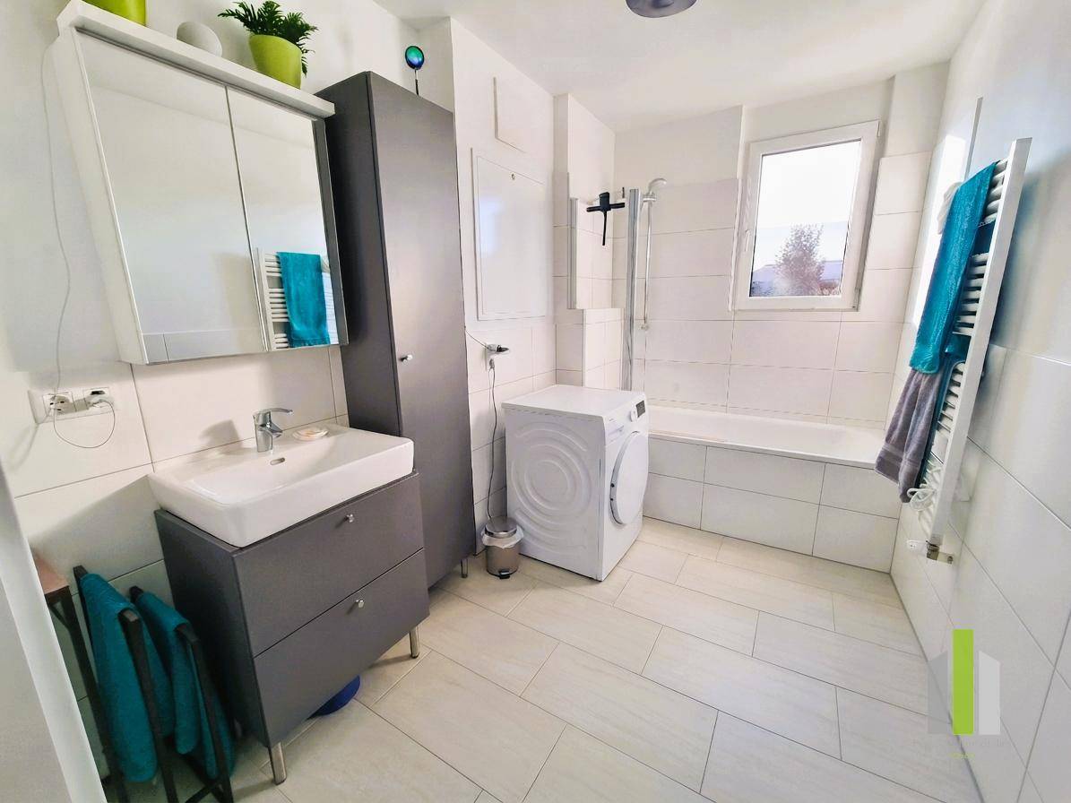 Modernes Badezimmer mit Badewanne, Dusche, Waschmaschine und Fenster für natürliche Belüftung und Helligkeit.