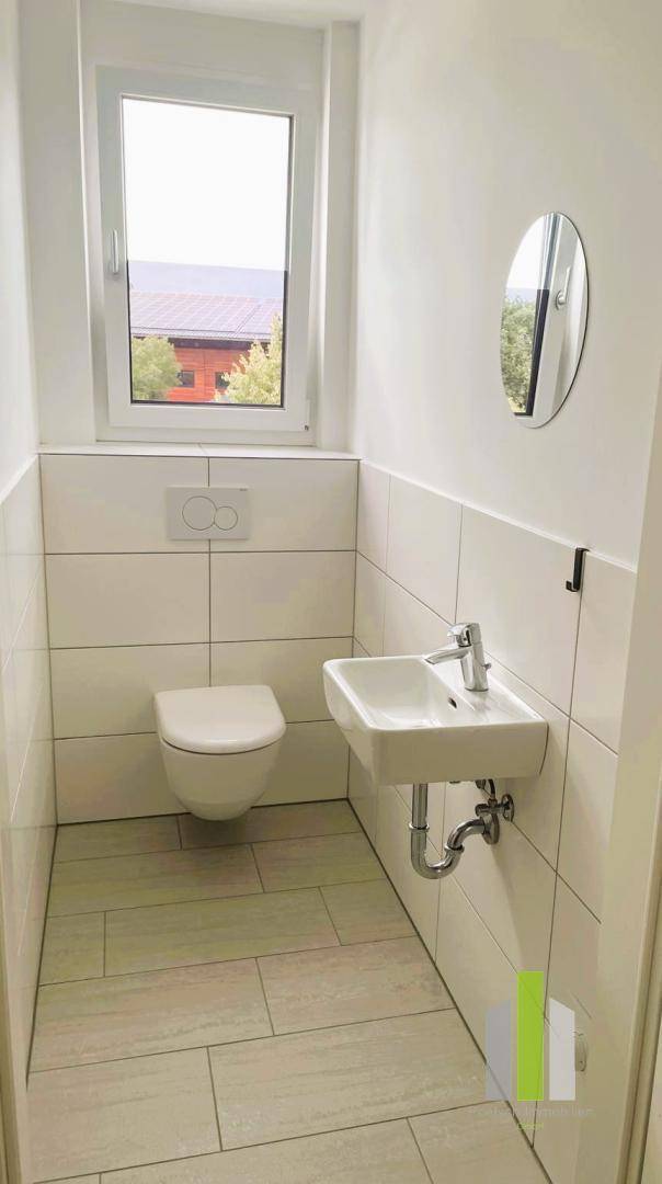 Separates WC mit wandhängender Toilette, kleinem Waschbecken und Fenster für optimale Belüftung.