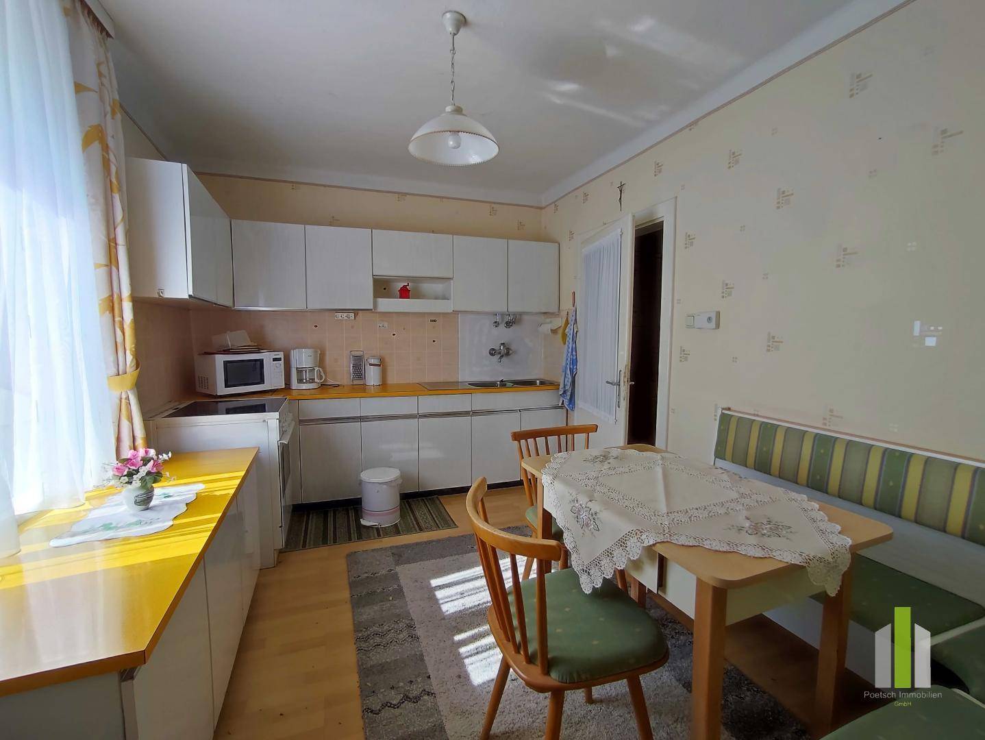 Funktionale Küche mit weißen Schränken, gelben Arbeitsplatten und einem Esstisch am Fenster.