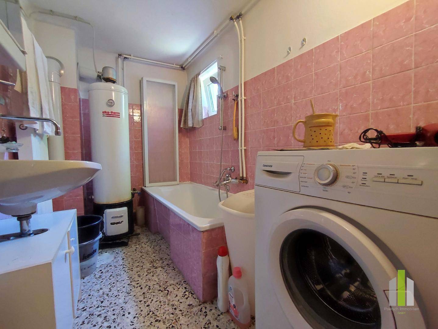 Badezimmer mit rosa Fliesen, Badewanne, Waschbecken und Waschmaschine, ausgestattet mit Boiler.