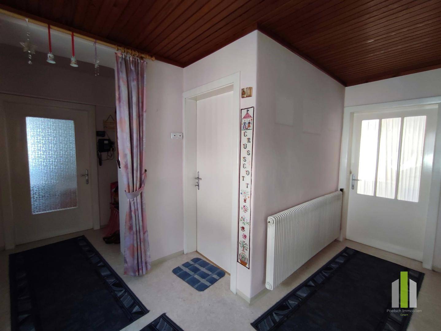 Heller Flur mit Holzdecke, Heizkörper und zwei Türen, die zu weiteren Räumen führen.