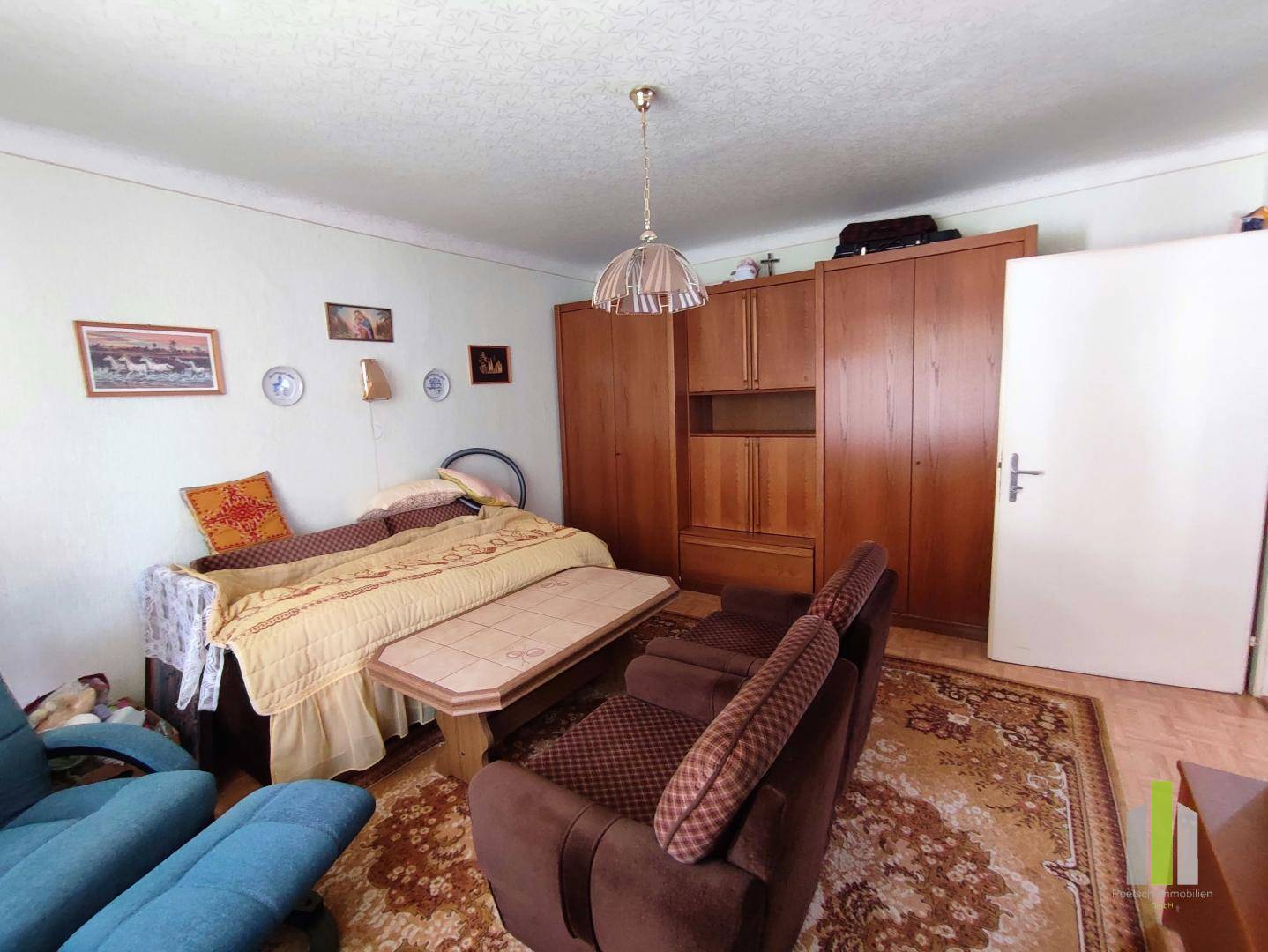 Helles Schlafzimmer mit Einzelbett, Holzschrank und traditionellem Teppich auf dem Boden.