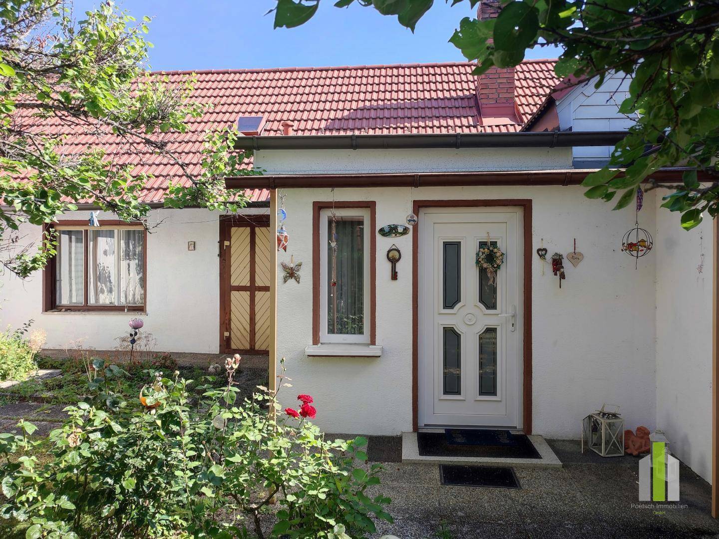 Eingangsbereich des Hauses mit rotem Ziegeldach, umgeben von blühenden Rosen und grünen Pflanzen.