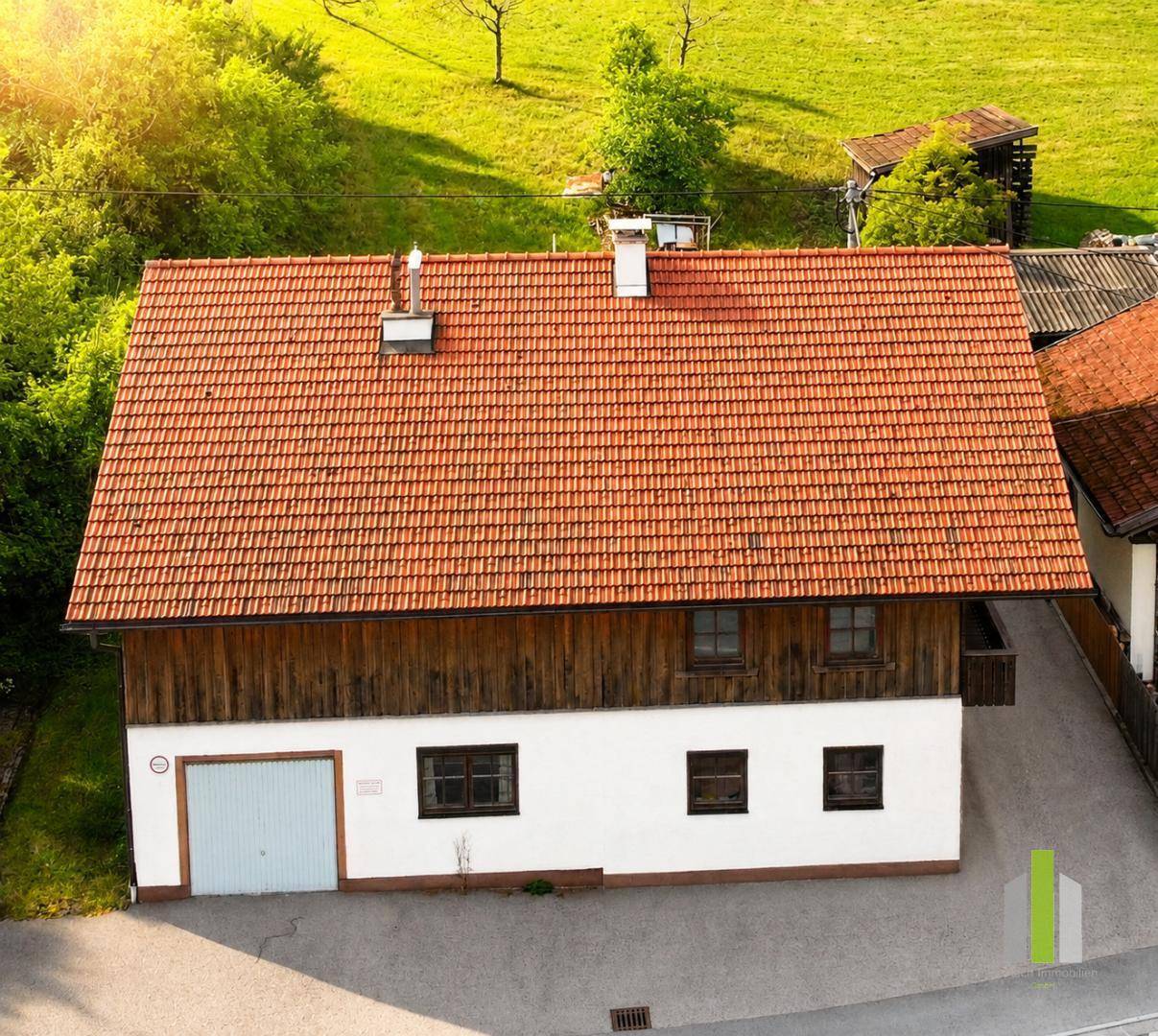 Vogelperspektive eines traditionellen Hauses mit rotem Ziegeldach und Holzelementen in ländlicher Umgebung.