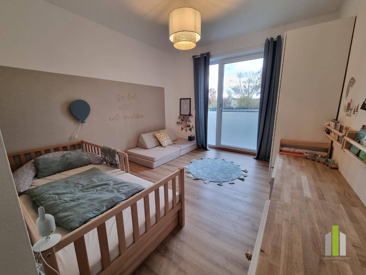 Helles Kinderzimmer mit Holzbett, kleiner Sitzecke und Zugang zu einem französischen Balkon.