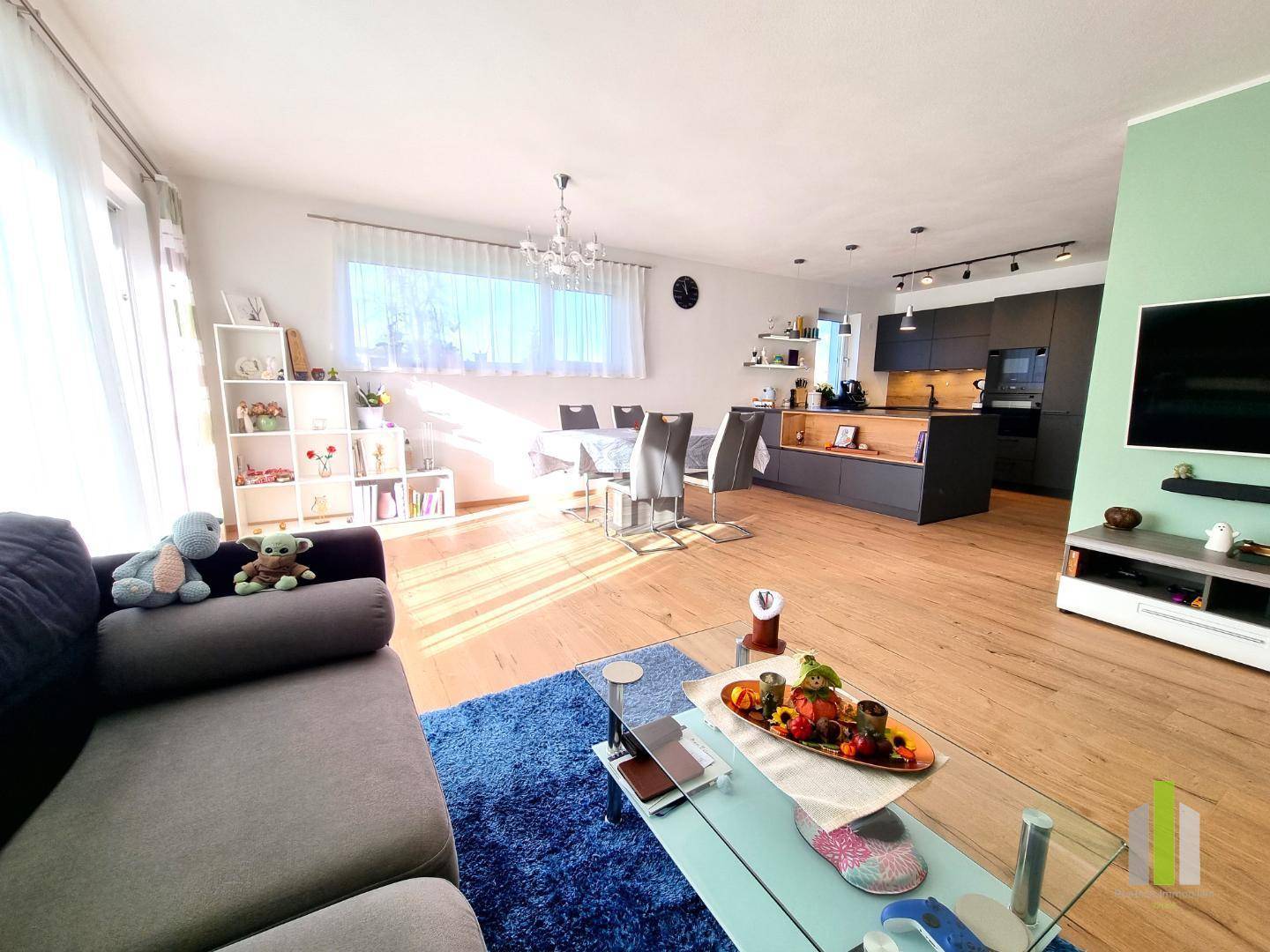 Heller, offener Wohn-Essbereich mit moderner Küche, Holzboden und viel Tageslicht.